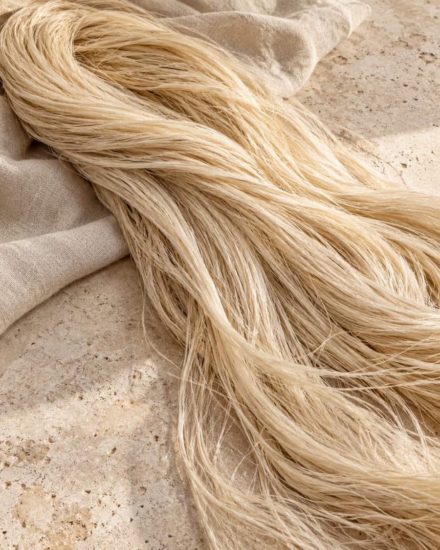 Long, pale golden agave fiber on linen and travertine