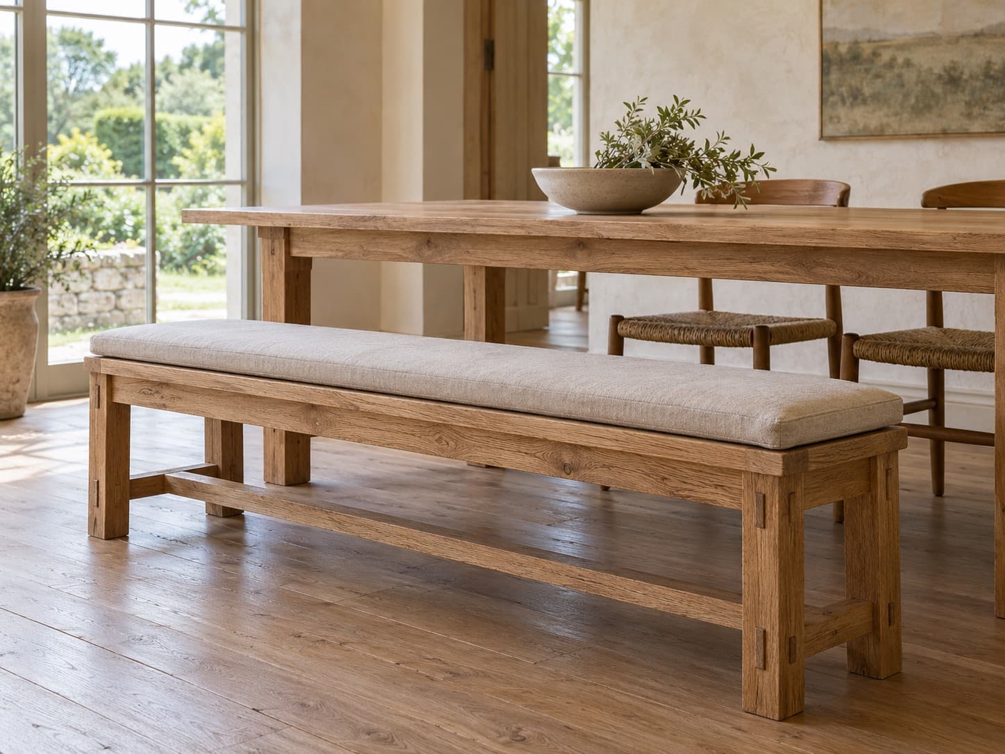 A long solid oak dining bench with a linen-covered cushion beside an oak table